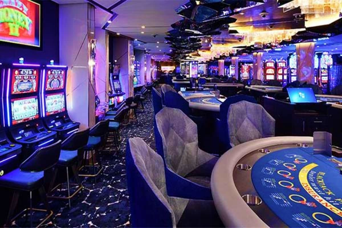 Modern casino floor with slot machines, gaming tables, and blue ambient lighting on Celebrity Edge cruise ship