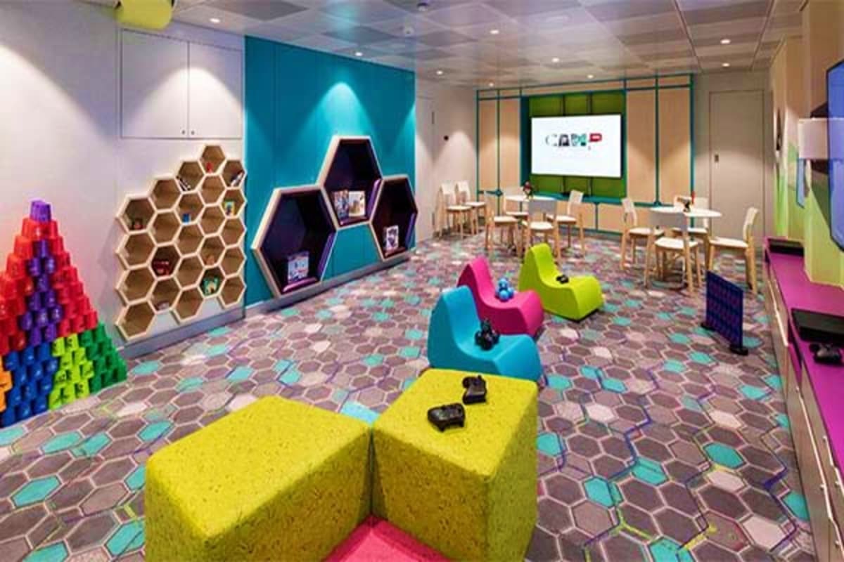 Modern cruise ship kids club playroom with colorful seating cubes, hexagonal storage wall, and gaming stations