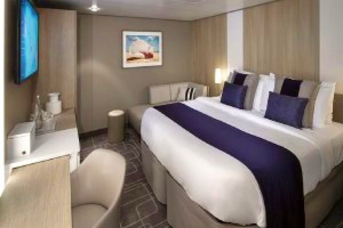 Celebrity Xcel Mediterranean Escape Modern cruise ship stateroom with queen bed, navy and white bedding, flat-screen TV, desk area, and contemporary beige and gr