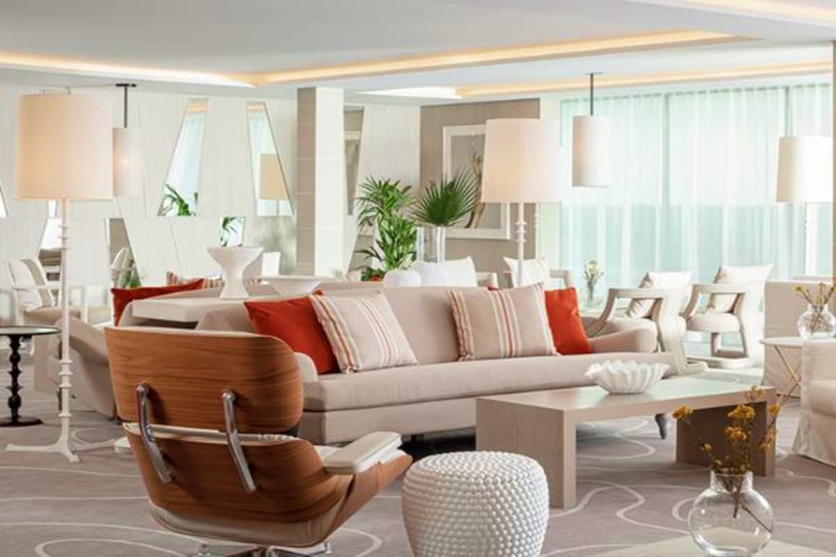 Modern luxury living room with beige sofa, wood accent chair, red pillows, pendant lights, and floor-to-ceiling windows overl