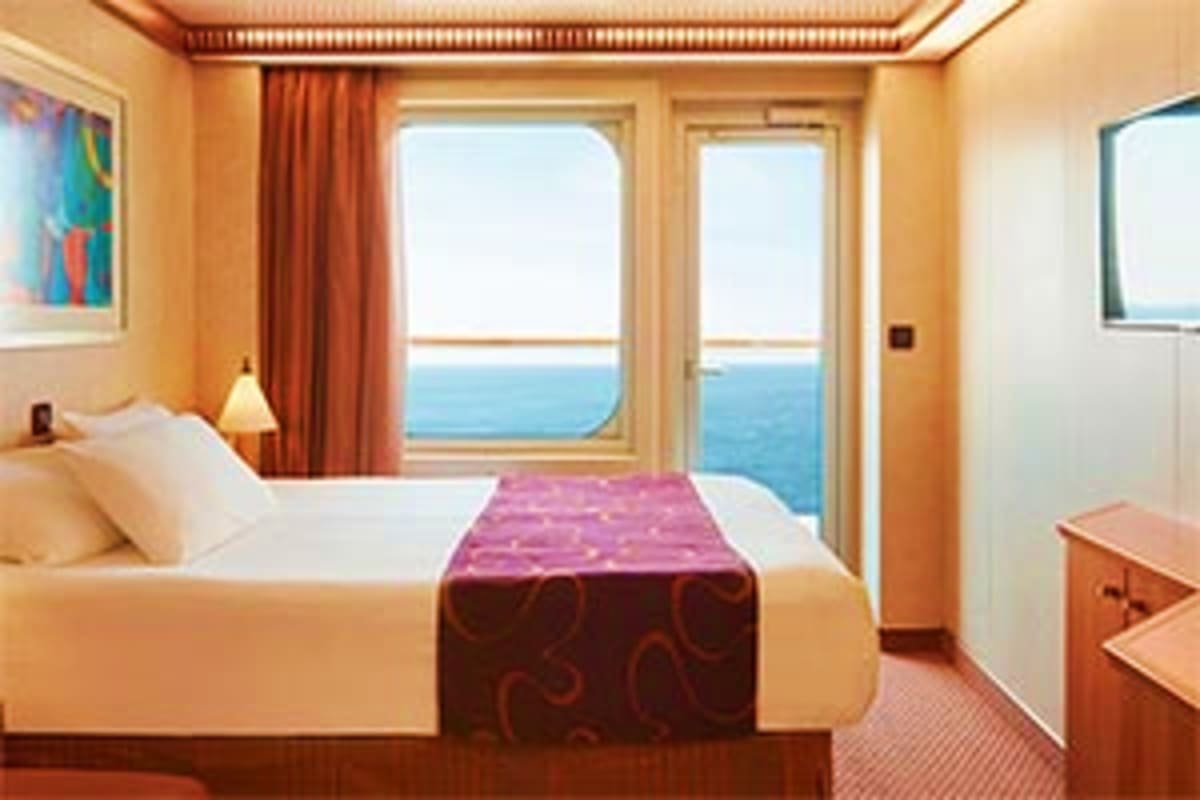 Luxury cruise ship cabin with ocean view balcony, queen bed with purple throw, cream walls, orange curtains, and sea horizon 