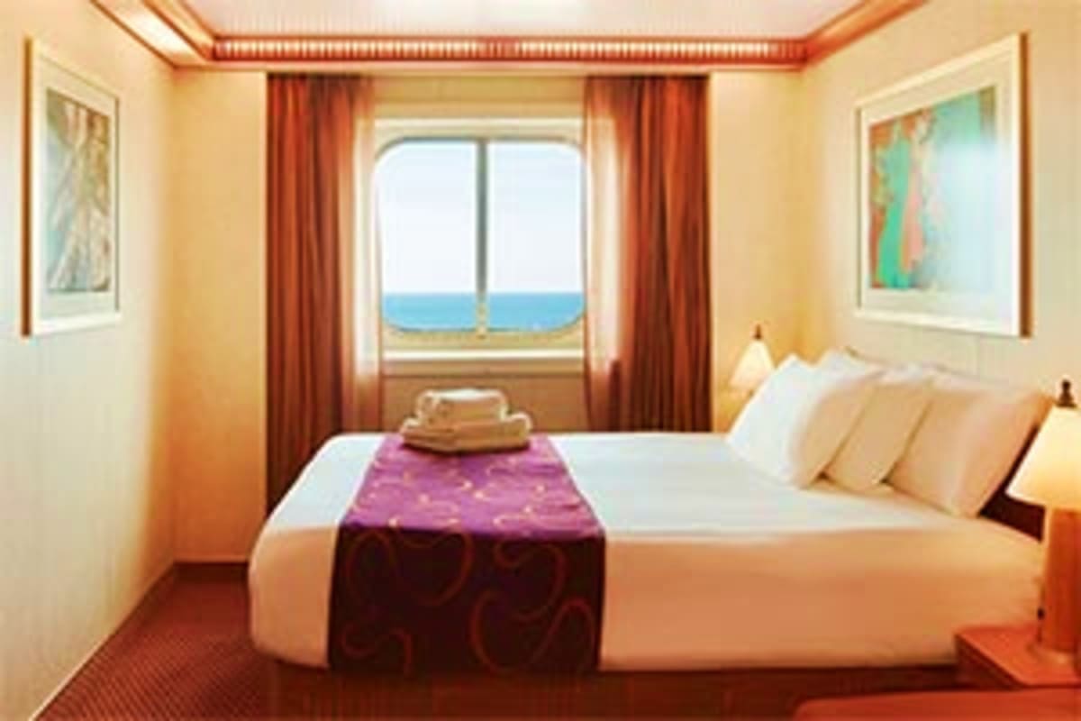 Luxury cruise ship cabin with ocean view through balcony window, queen bed with purple runner, warm lighting and red curtains