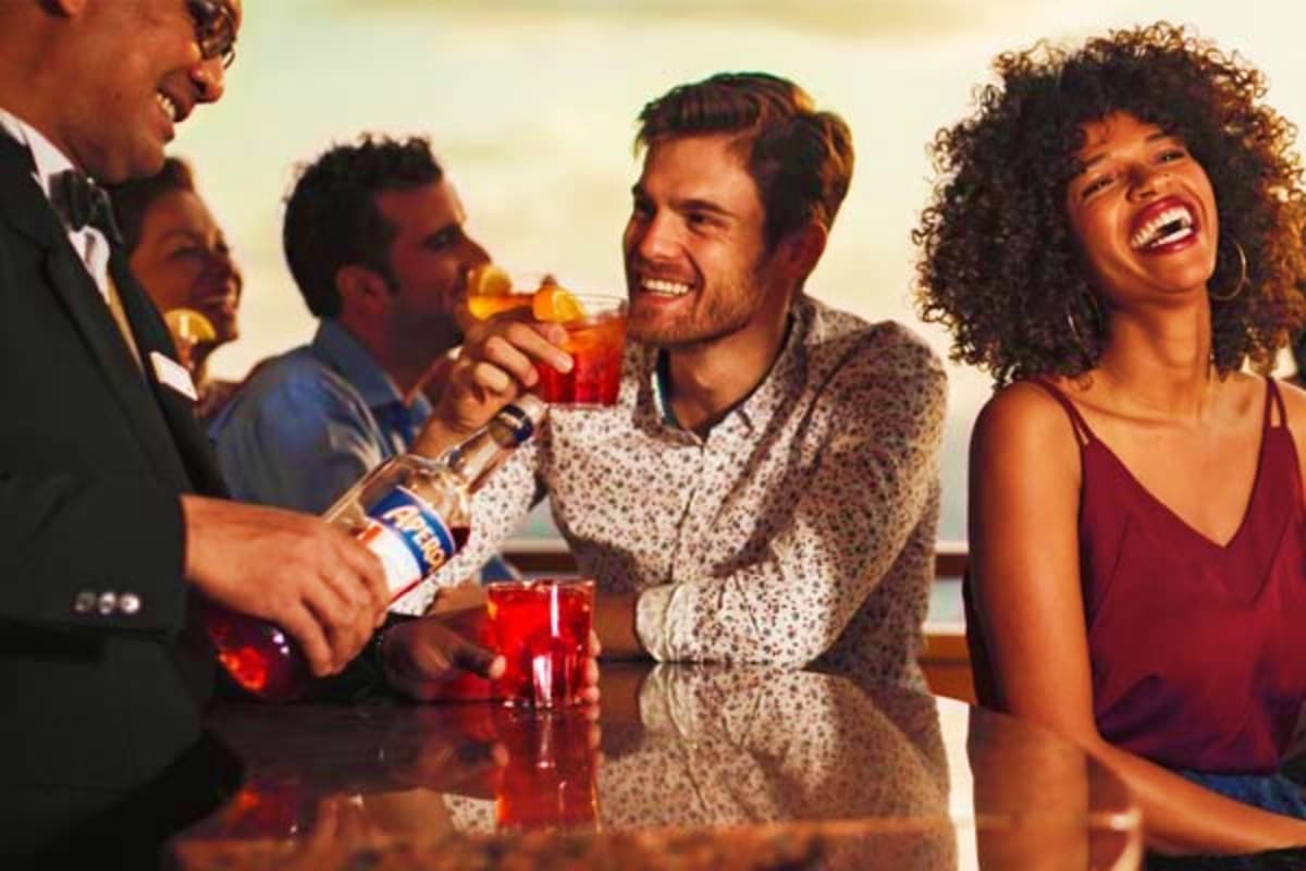 Group of friends enjoying drinks and laughing together at an outdoor bar on a cruise ship deck at sunset
