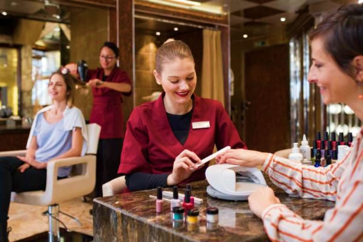 Professional spa receptionist in maroon uniform assists smiling female guest at marble counter with nail polish display and s