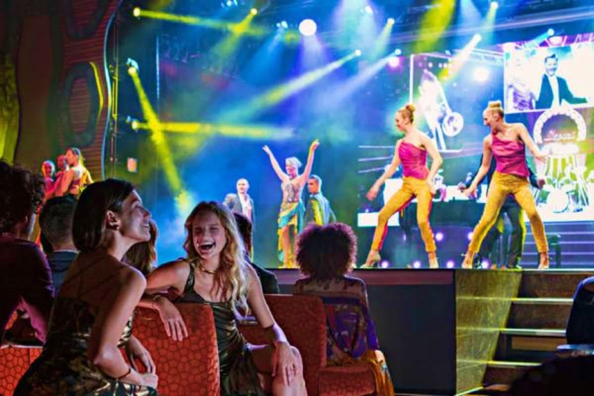 Audience members enjoying a live stage performance with dancers in colorful costumes on a cruise ship entertainment venue