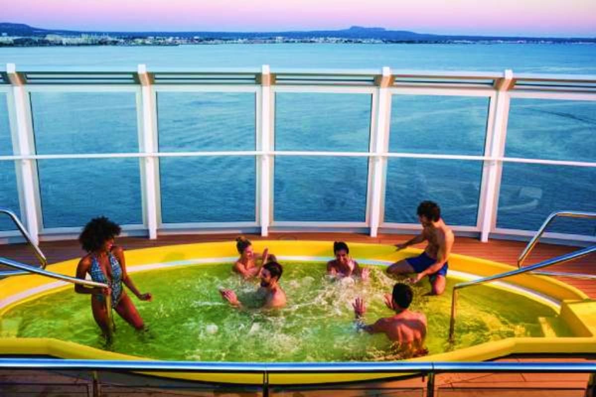 Family enjoying colorful pool deck with ocean and coastline view on cruise ship during sunset