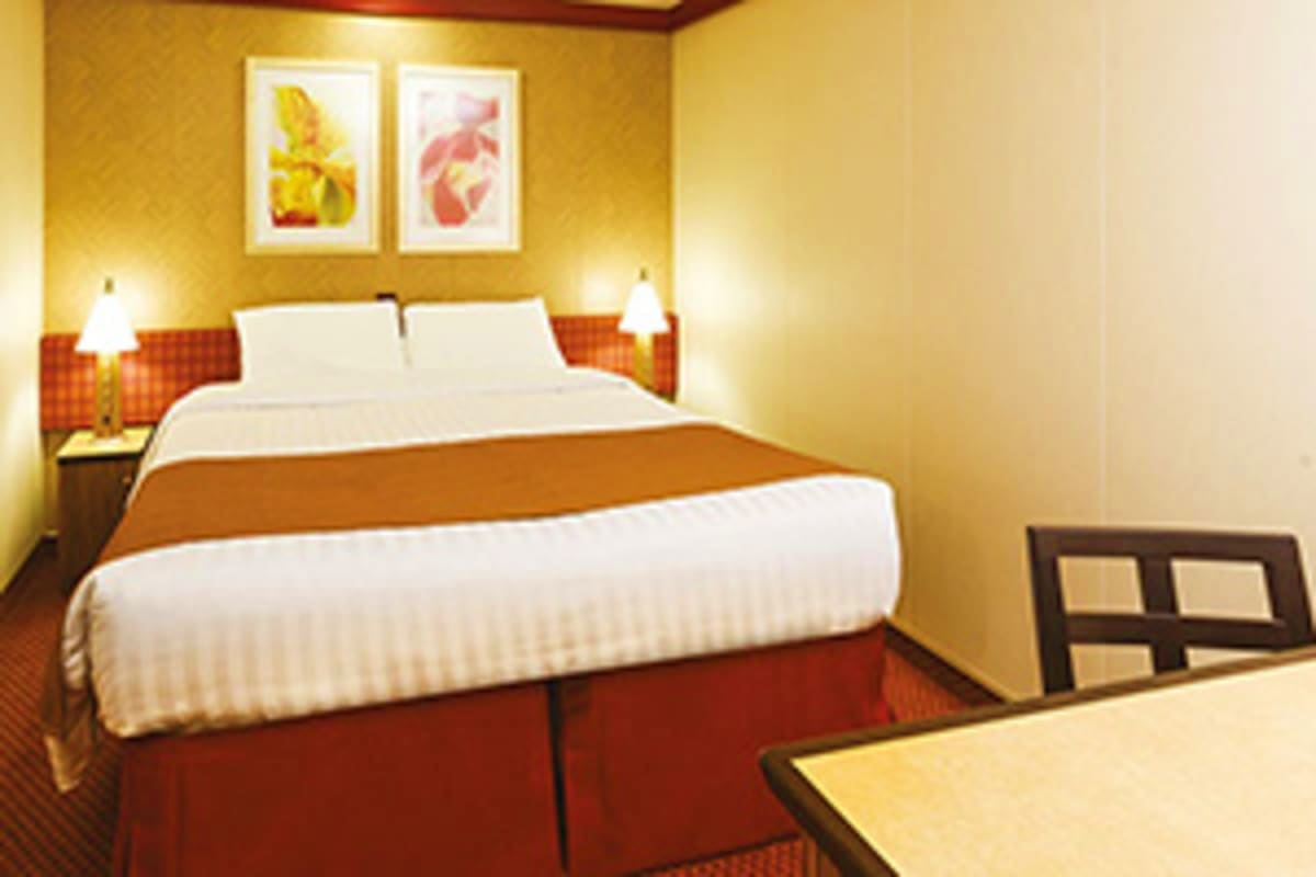 Modern hotel bedroom with queen bed, white pillows, orange bed runner, yellow walls, framed botanical artwork, bedside lamps,