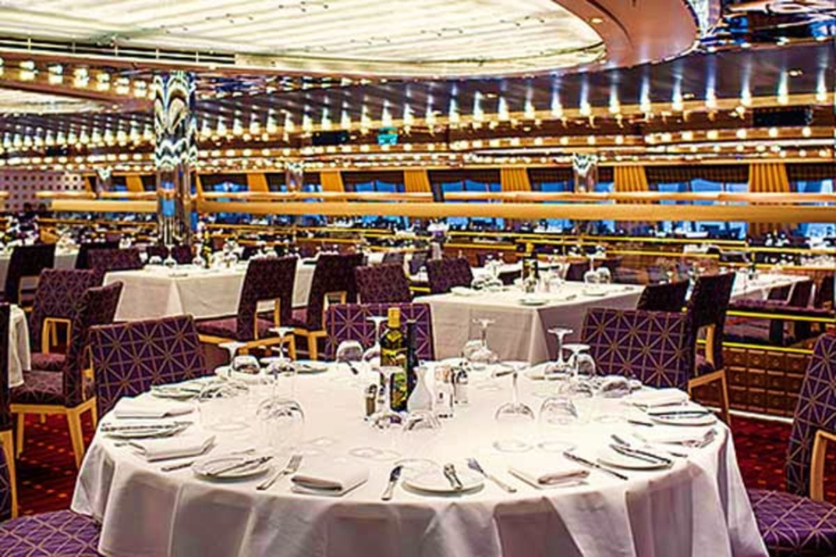 Elegant dining room on Costa Diadema cruise ship with round tables, white linens, and formal place settings beneath ornate ce