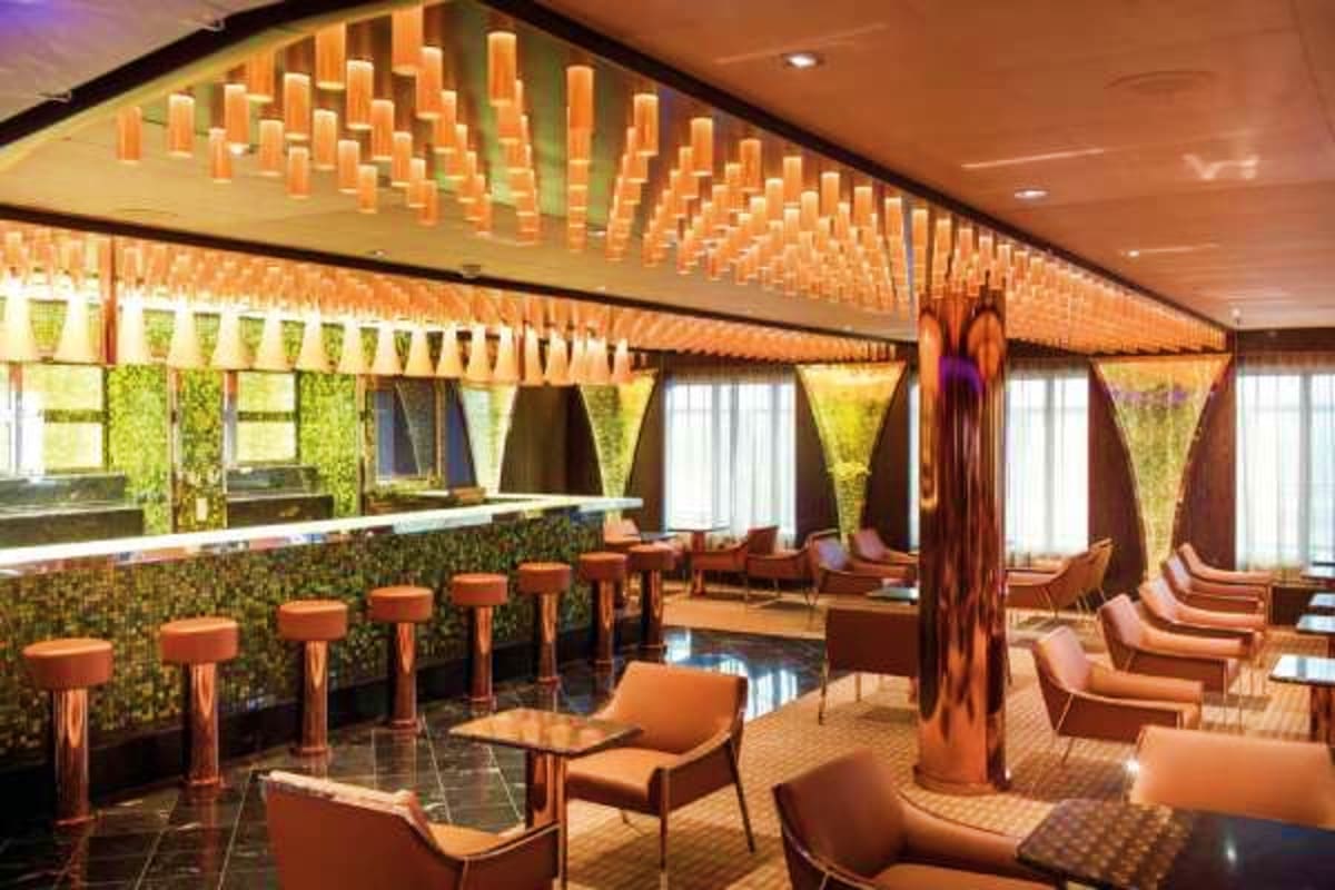 Modern lounge bar with orange seating, green moss wall panels, wooden ceiling details, and natural light from floor-to-ceilin