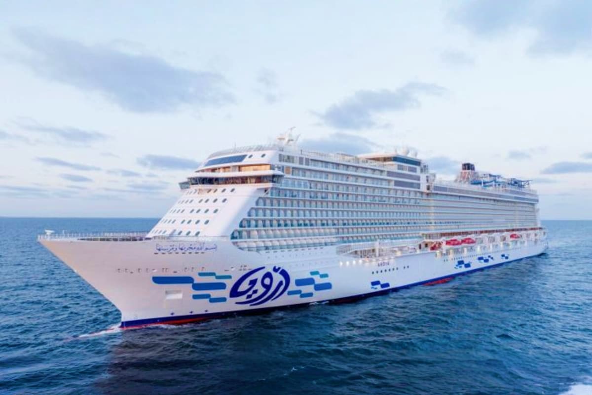 Large modern cruise ship with blue and white hull sailing on open ocean under cloudy sky
