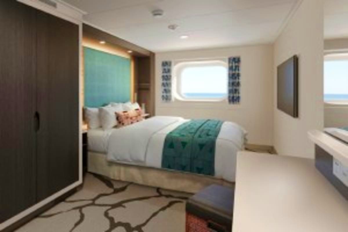 Modern cruise ship cabin with queen bed, turquoise headboard, porthole window overlooking ocean, dark wood closets, and patte
