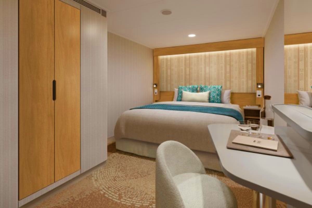 Modern cruise ship cabin with queen bed, teal accents, wooden wardrobe, white desk with chair, and contemporary furnishings