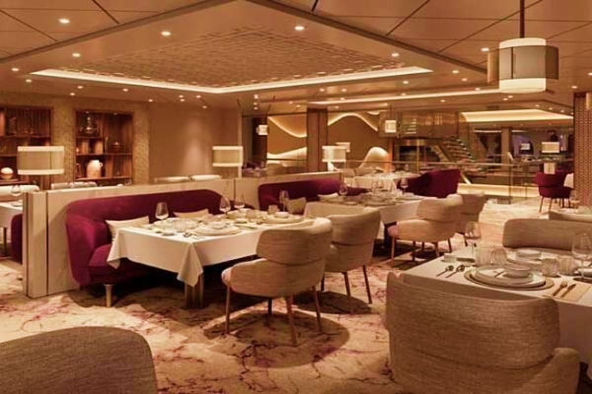Elegant cruise ship dining room with burgundy booth seating, beige chairs, white-clothed tables, and warm ambient lighting th