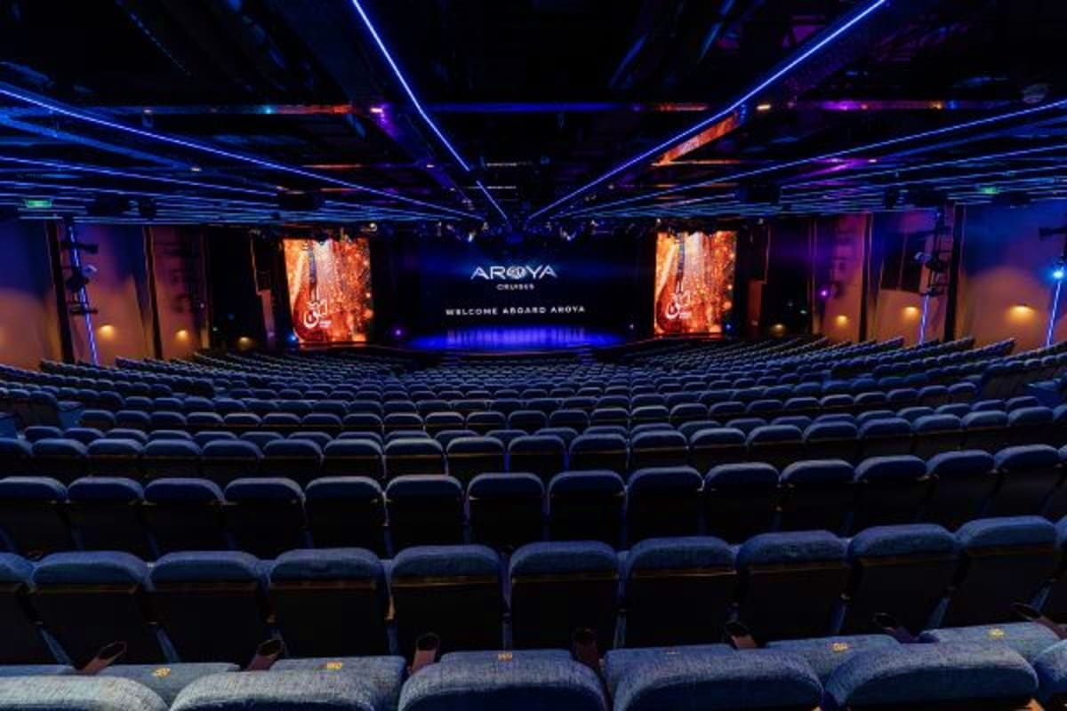 Modern cinema theater interior with blue and purple LED lighting, rows of dark seats, and Aroya branding on central screen di