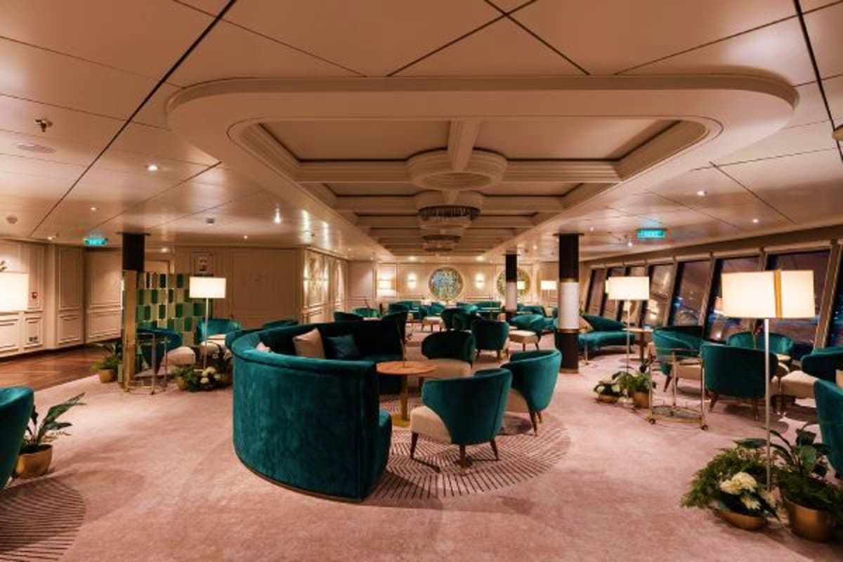 Luxury cruise ship lounge with teal curved seating, coffered ceiling, and ocean view windows