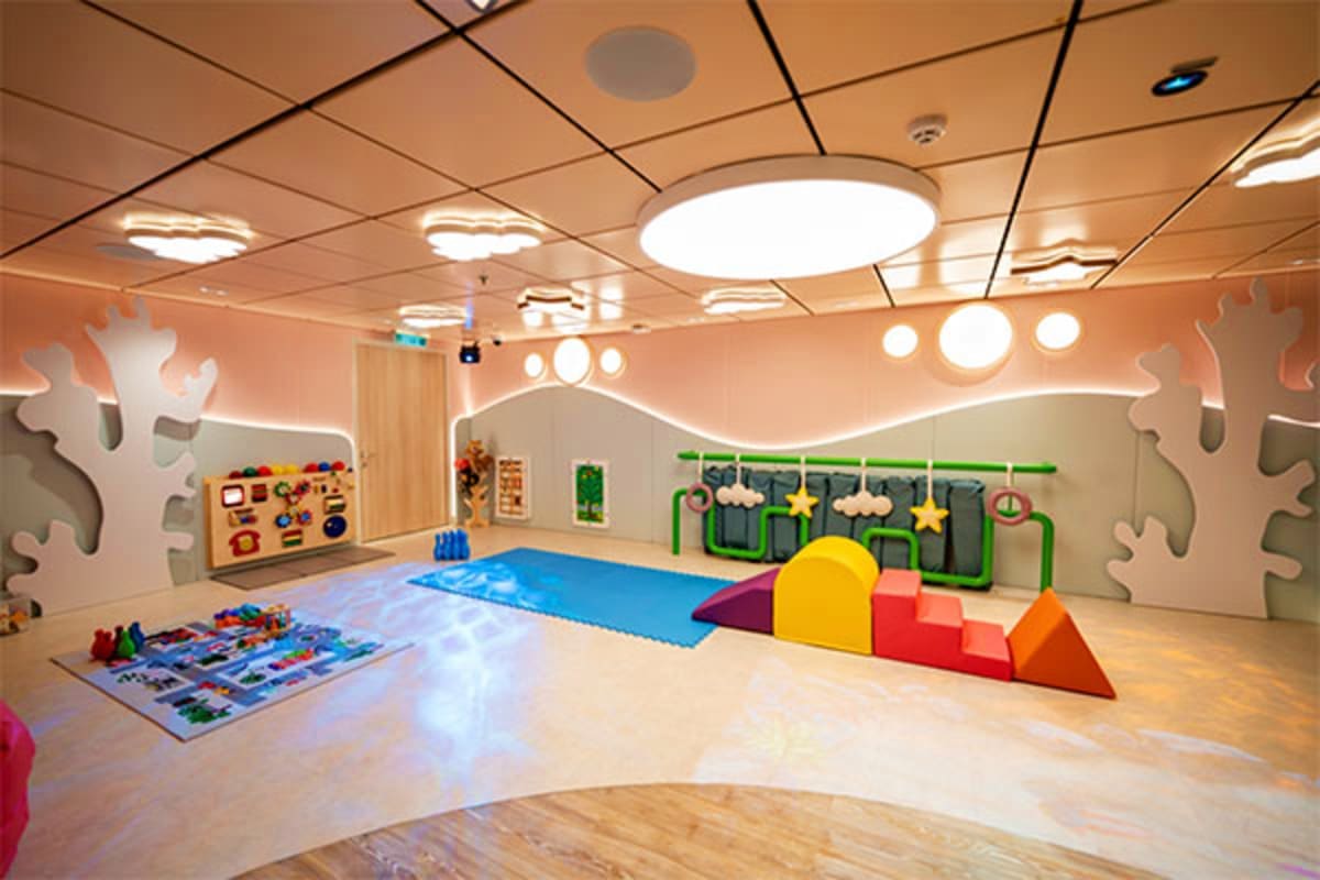 Modern children's play room with colorful foam climbing blocks, blue mat, activity wall, and decorative hanging elements on c