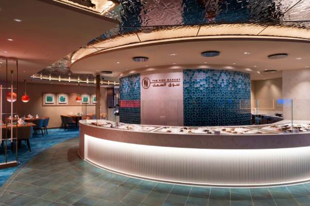 Modern seafood restaurant interior with curved illuminated counter, blue tiled accent wall, dining area with red pendant ligh