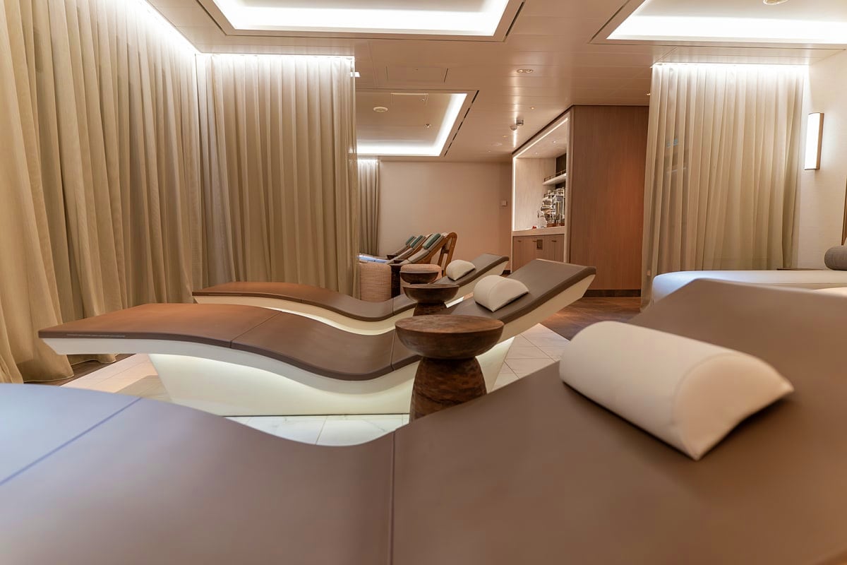 Modern spa relaxation room with curved lounge chairs, wooden accents, soft lighting, and floor-to-ceiling curtains on Aroya A