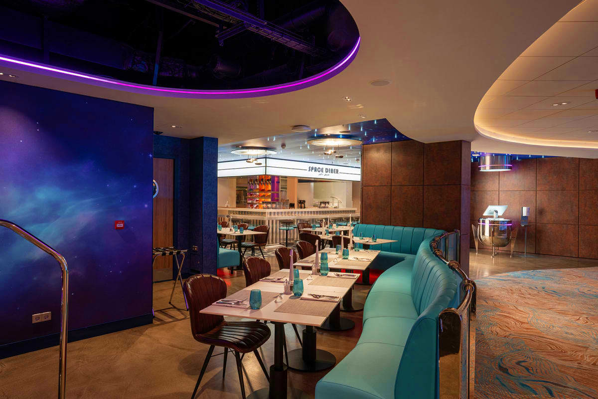 Modern restaurant interior with turquoise booth seating, brown chairs, dining tables, purple cosmic wall art, and illuminated