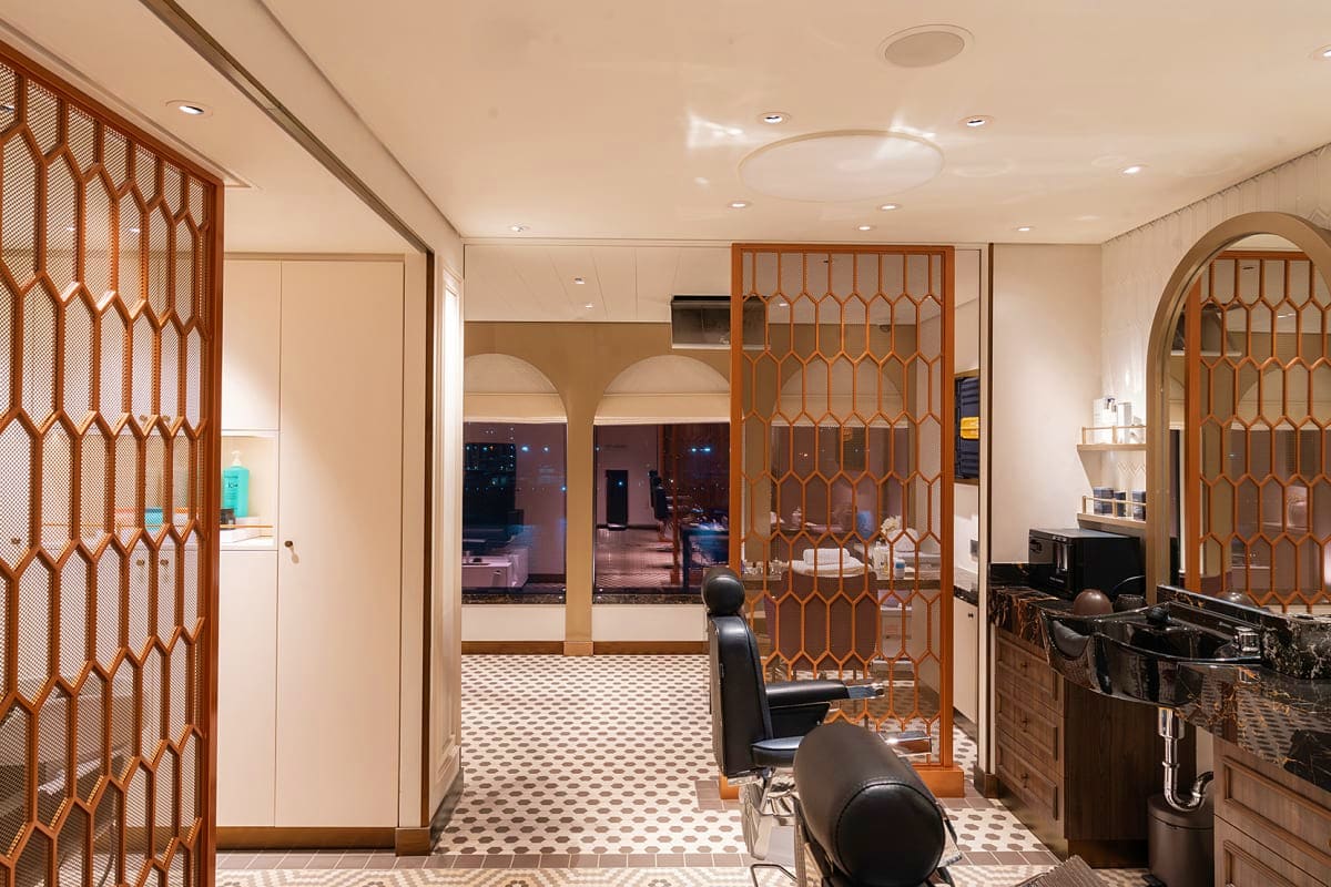 Modern cruise ship cabin interior with wooden geometric room dividers, cream walls, recessed lighting, and contemporary furni