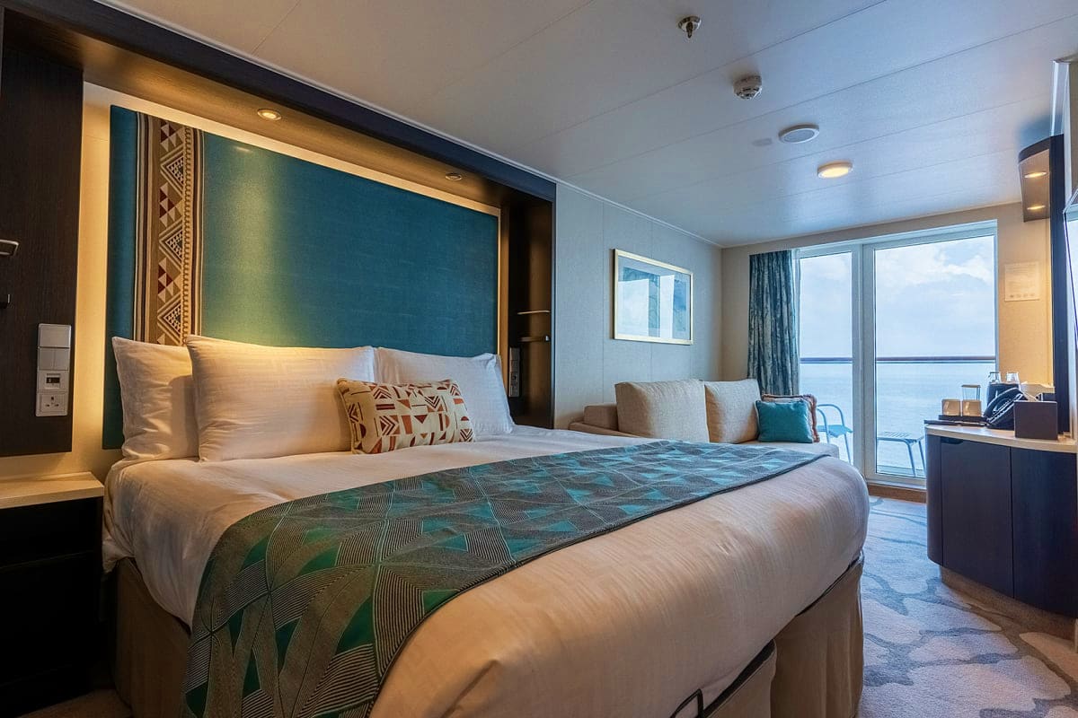 Luxury cruise ship stateroom with teal accent wall, king bed with ocean view balcony and seating area