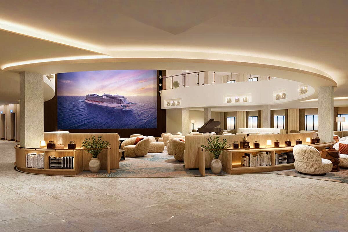 Luxury cruise ship atrium lounge with curved ceiling lighting, cream furniture, wooden shelving, and large screen displaying 