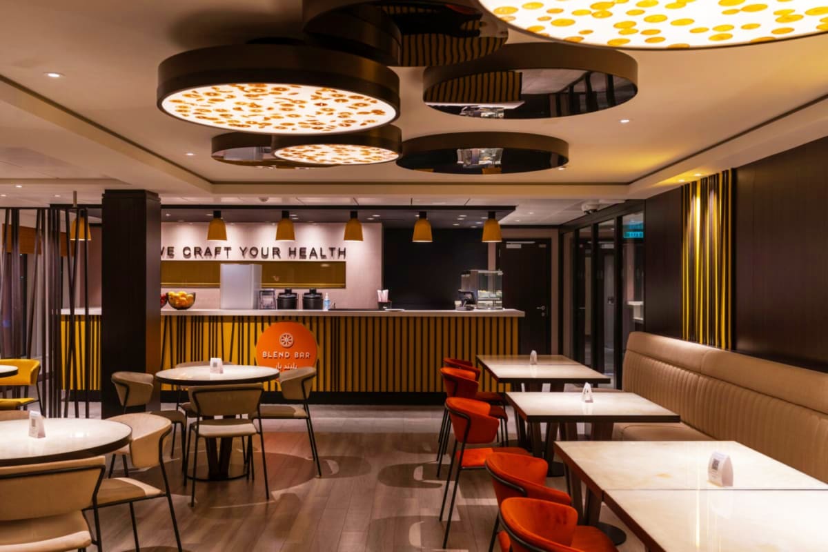 Modern health-focused blend bar restaurant with yellow and black striped design, white tables, orange chairs, and illuminated