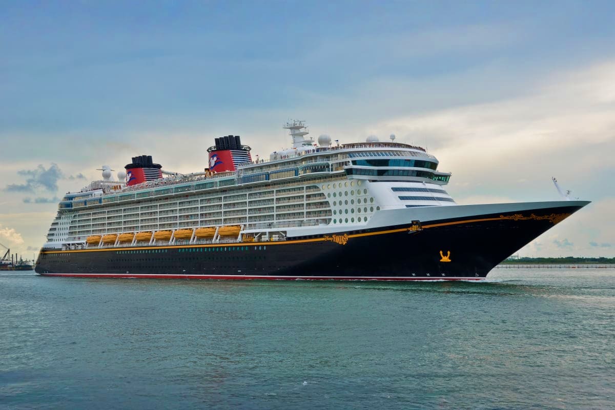 Large modern cruise ship with black hull and white superstructure sailing on turquoise water under cloudy sky