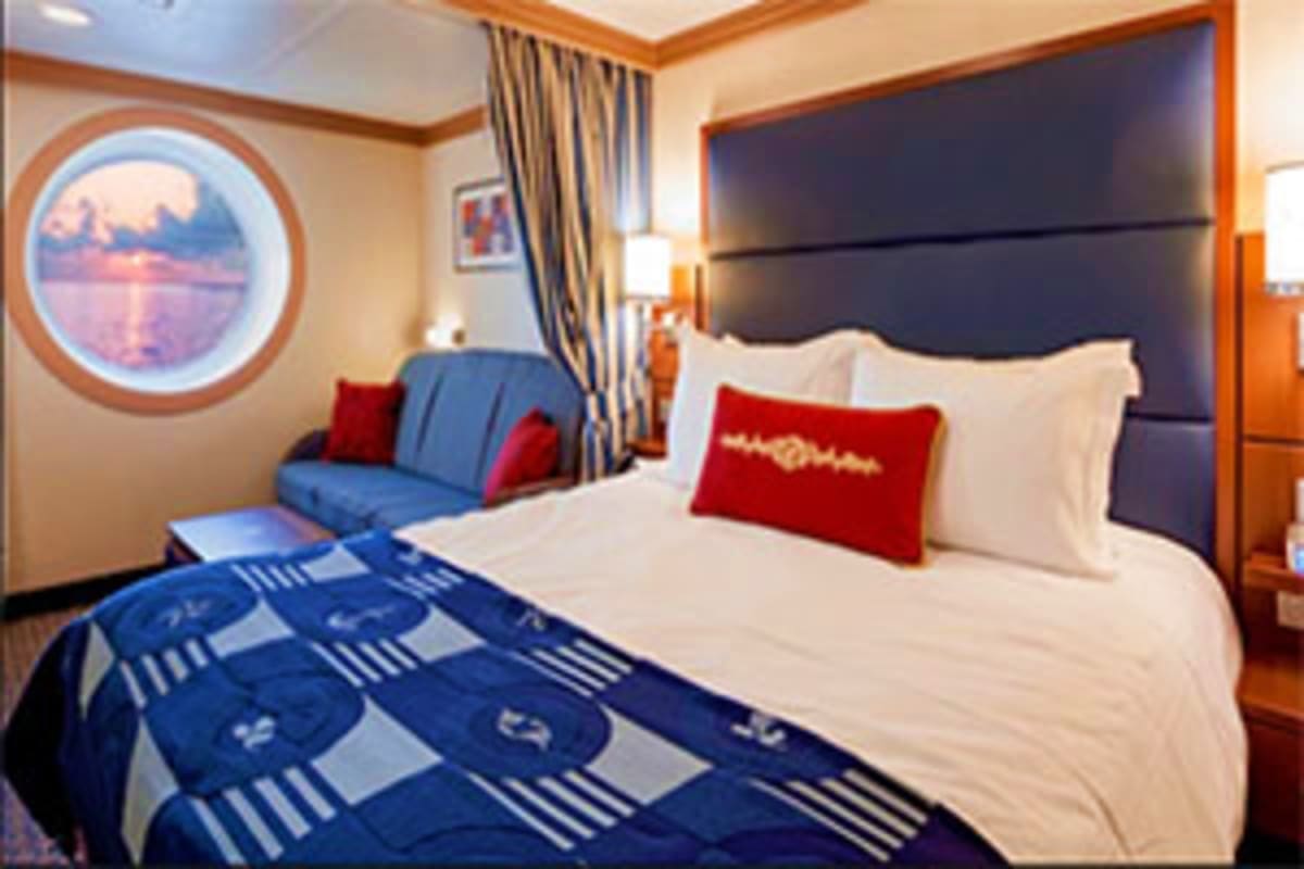 Luxurious cruise ship stateroom with queen bed, black headboard, white linens, red and white pillows, blue patterned throw bl
