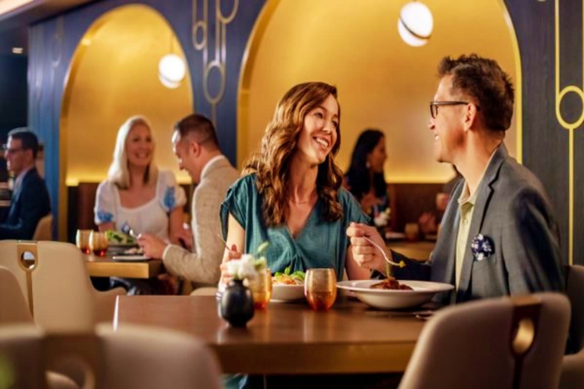 Couple dining together at an upscale restaurant with golden arch lighting and other guests in background on Disney cruise shi