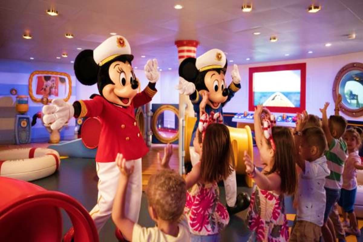 Mickey and Minnie Mouse in captain uniforms greet children in a ship's indoor venue decorated with nautical themes and portho