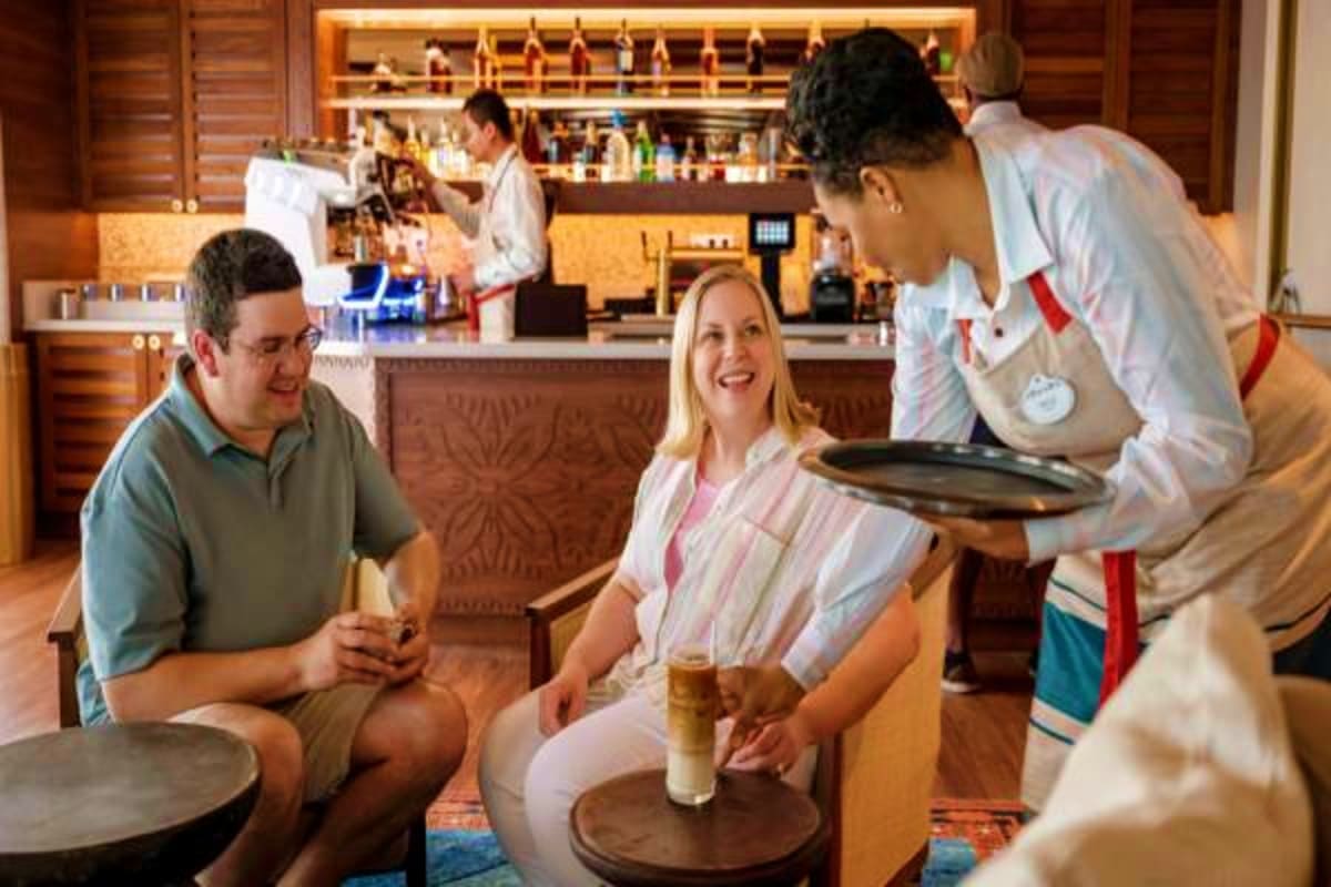 Restaurant staff serving drinks to smiling guests in an upscale dining venue with wood paneling and bar shelving