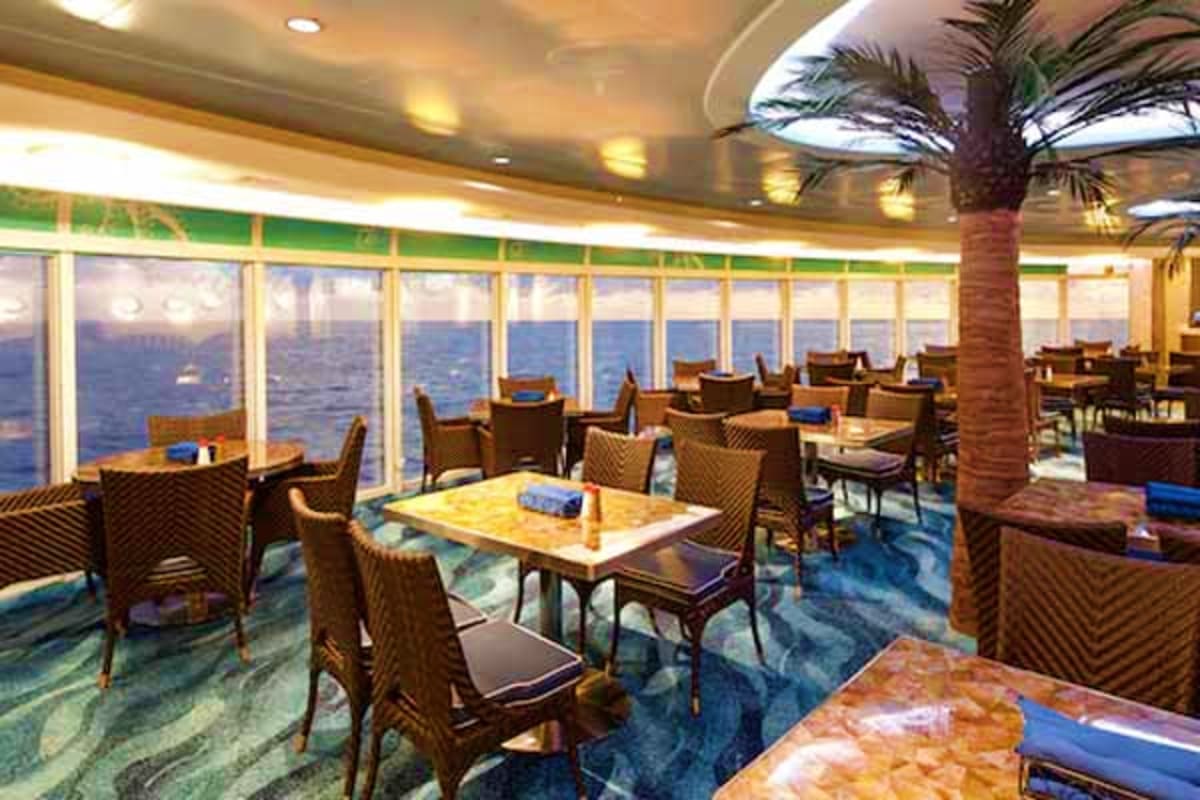 Elegant dining room on Disney Dream cruise ship with floor-to-ceiling ocean views, wooden chairs, and palm tree decoration