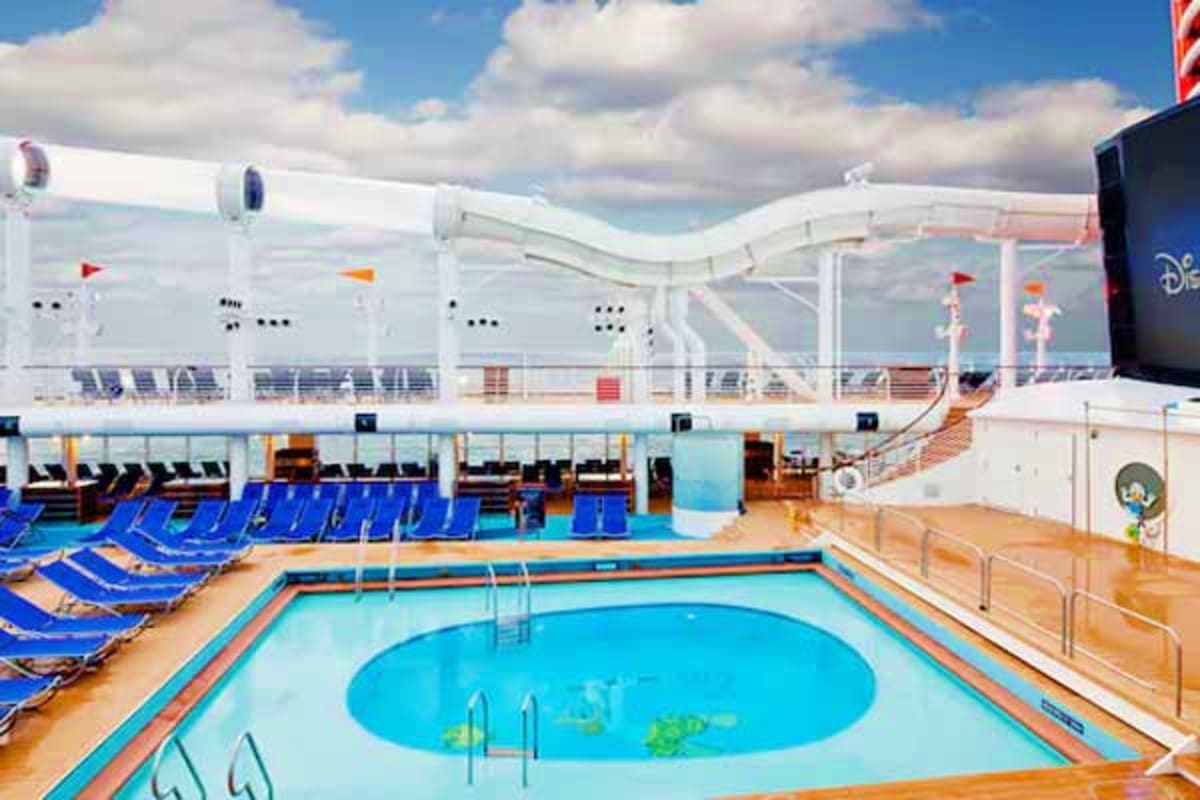 Disney cruise ship pool deck with bright blue swimming pool, lounge chairs, and ocean view under cloudy sky