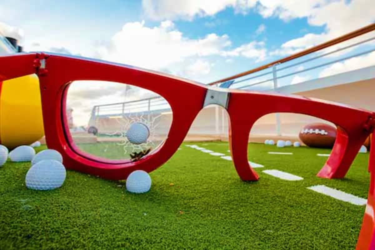 Oversized red glasses sculpture on artificial turf with golf balls and football, representing sports and recreation activitie