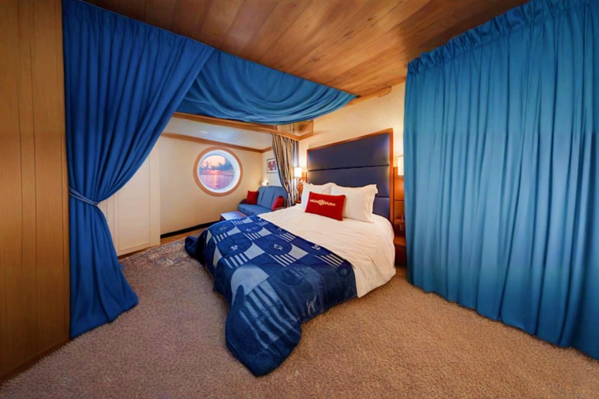 Luxurious cruise ship cabin with blue draped curtains, queen bed with white linens, wooden ceiling, and circular porthole win