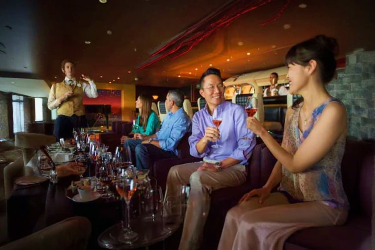 Group of adults enjoying cocktails and socializing in an upscale cruise ship lounge with warm lighting and modern décor.