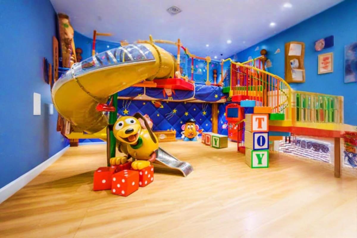 Colorful indoor children's play area with yellow airplane slide, toy blocks spelling "TOY", red dice, and space-themed decora