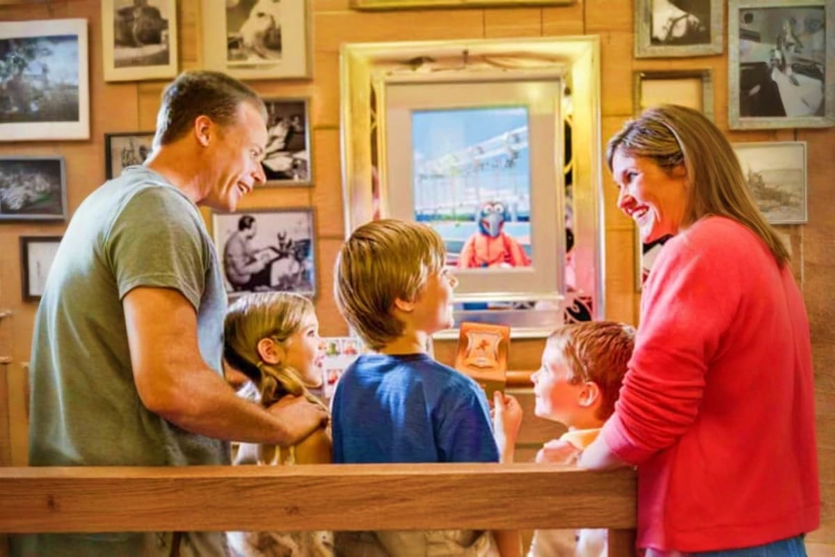 Family with two children visiting Disney Dream cruise ship museum exhibit with framed photographs on wood-paneled walls and s