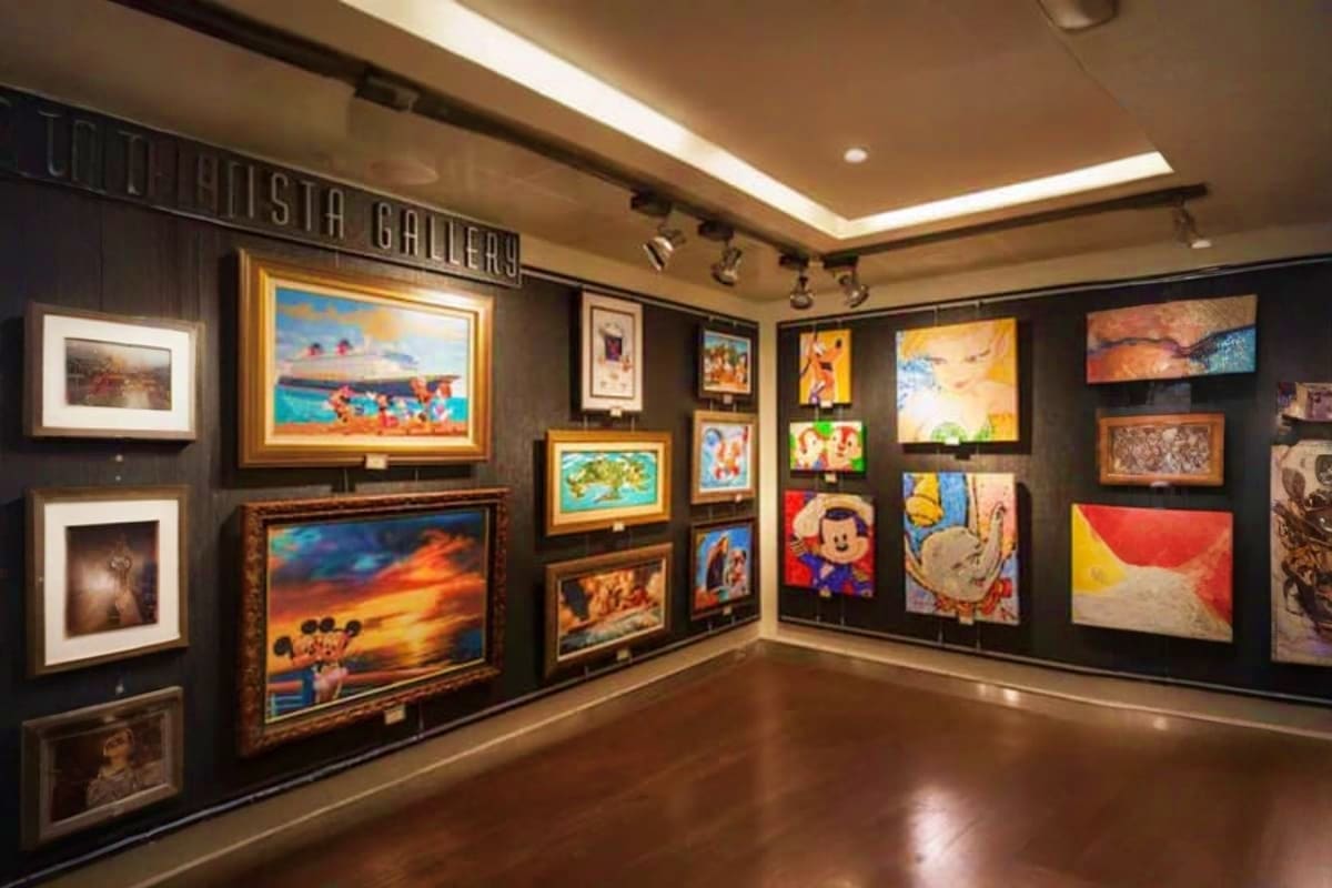 Interior of art gallery with framed paintings and artwork displayed on dark walls, wooden floor, and ceiling lighting
