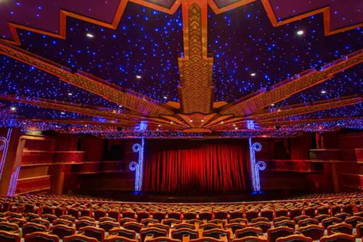 Grand ornate theater interior with red velvet seats, red curtains on stage, and blue starlit ceiling with golden architectura