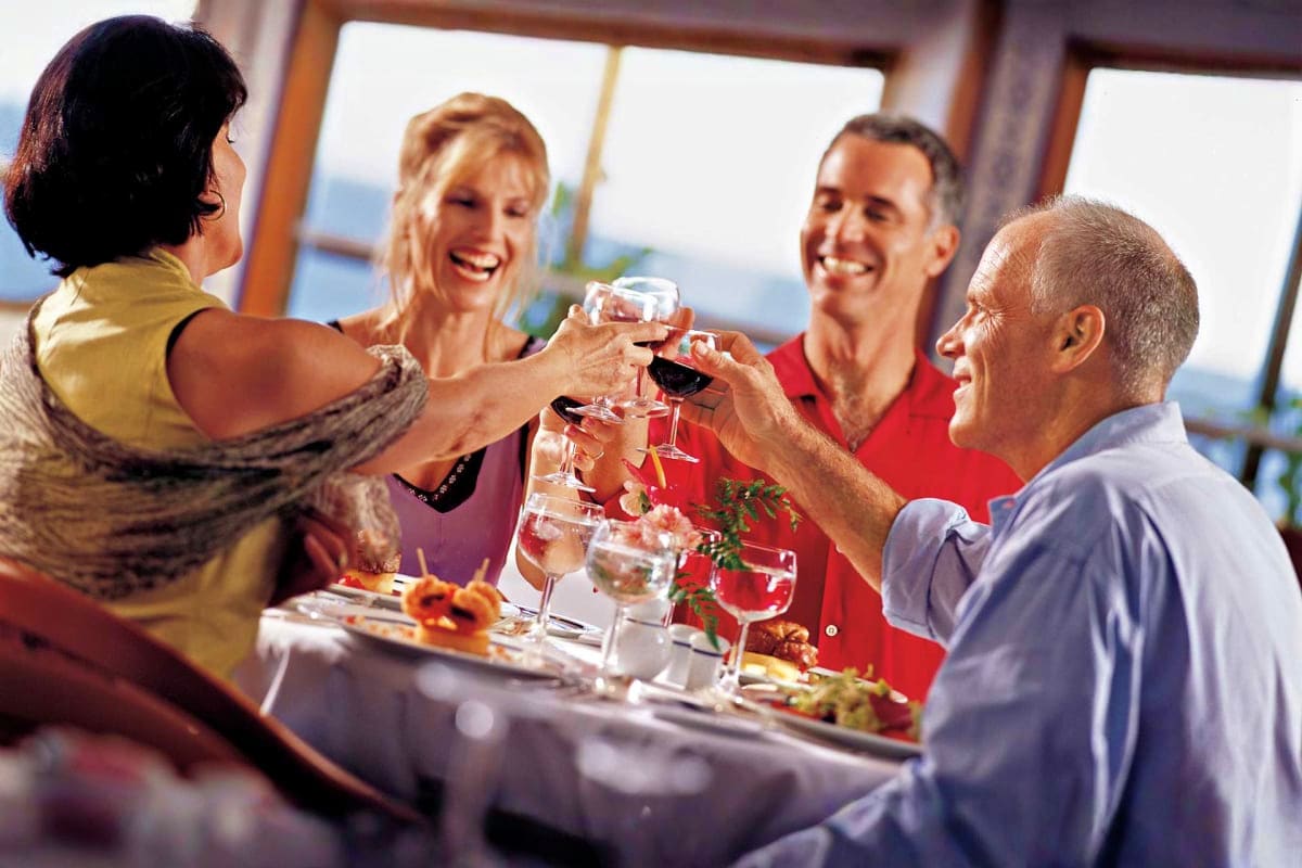 Group of four adults toasting with wine glasses at a formal dinner table on a cruise ship with ocean view windows