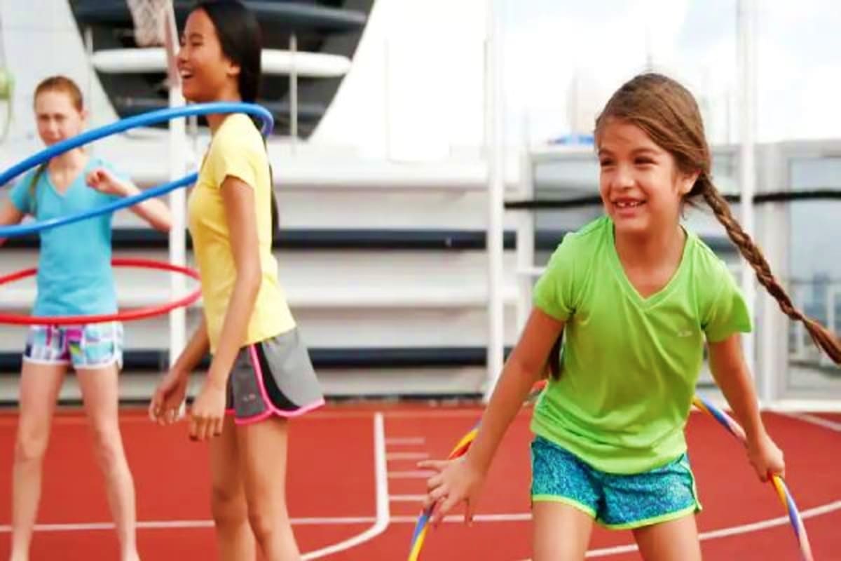 Children playing with hula hoops and jump ropes on a red sports court aboard a cruise ship