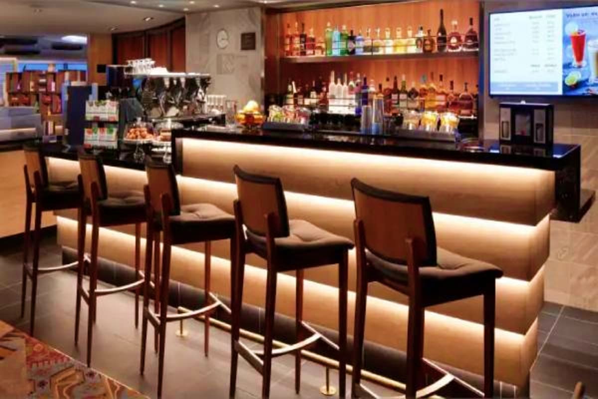 Oosterdam Mediterranean Voyage Modern cruise ship bar with illuminated counter, wooden bar stools, and shelves of colorful liquor bottles against orange acc