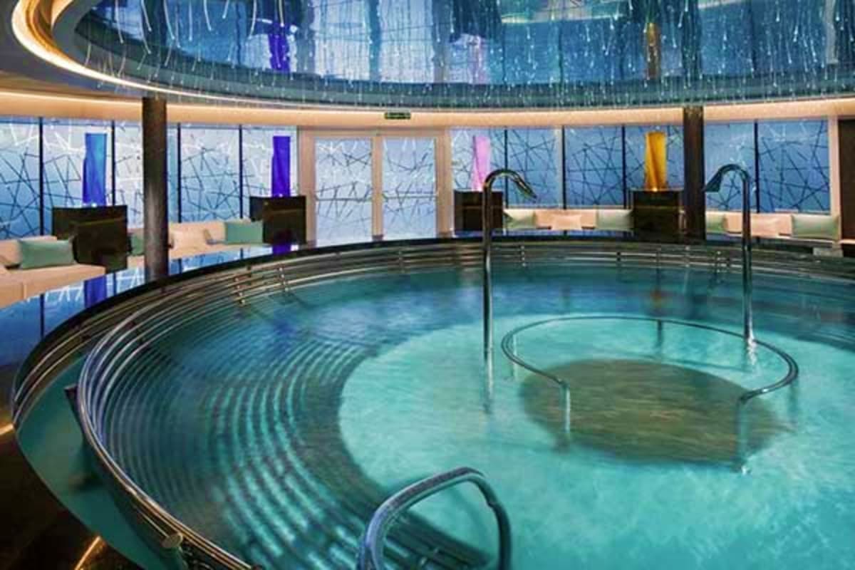 Luxury spa pool with curved glass railings, turquoise water, and floor-to-ceiling windows overlooking the sea on cruise ship 