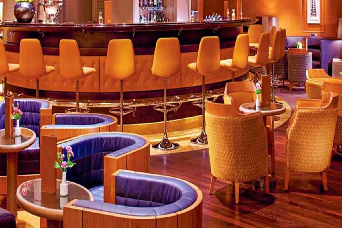 Elegant ship lounge with curved booth seating, orange upholstered chairs, dark wood bar counter, and ambient lighting on Oost