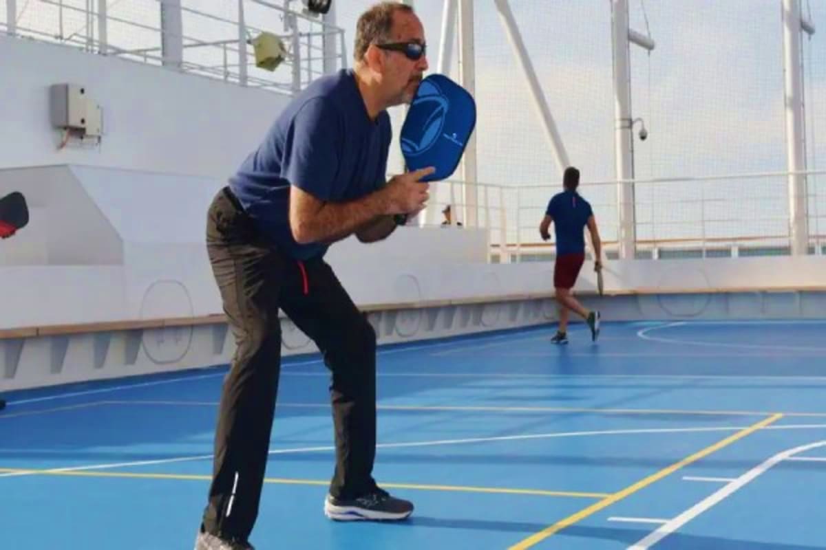 Man playing paddleball on the blue sports court of a cruise ship with another player in the background