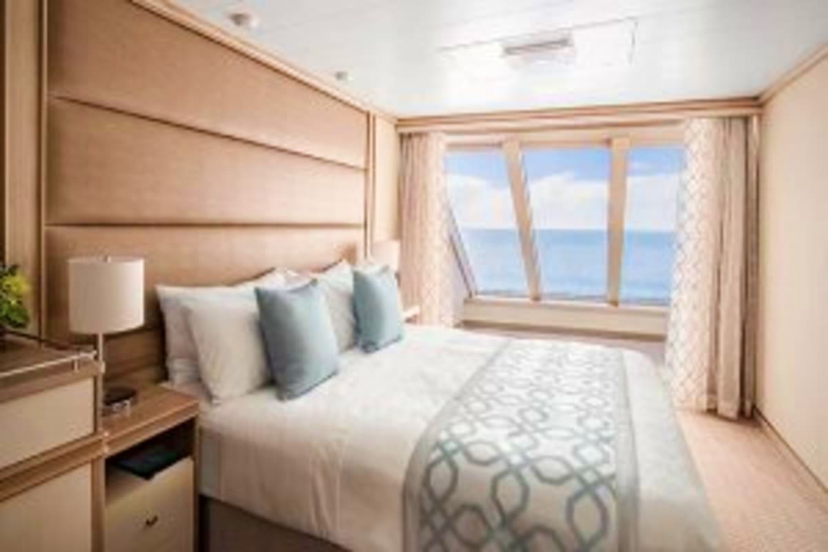 Luxurious cruise ship stateroom with ocean view windows overlooking the Aegean Sea, featuring a queen bed and modern amenitie