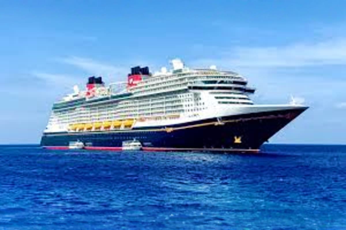Large Disney cruise ship with white upper decks and dark blue hull sailing on blue ocean water under clear sky