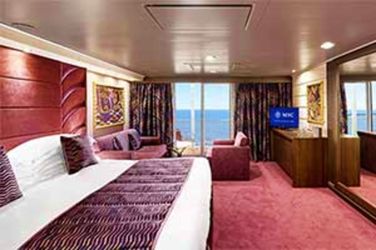 MSC Preziosa Northern Escape Luxury cruise ship suite with queen bed, sitting area, and panoramic ocean views through floor-to-ceiling windows on MSC Prez